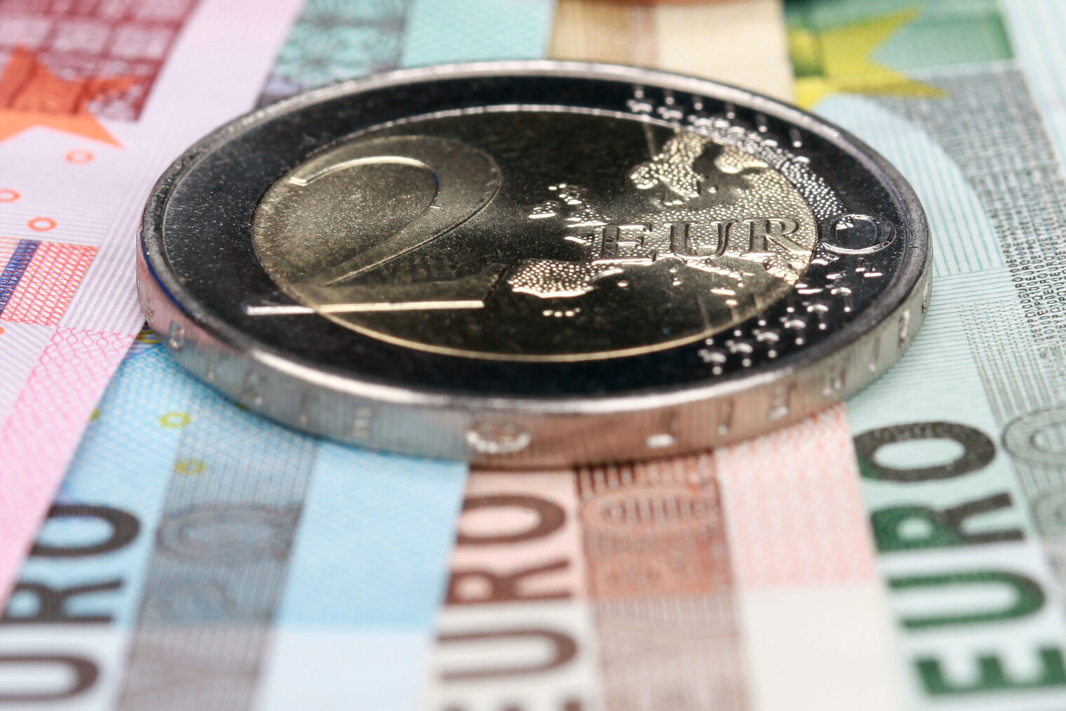 Eine 2-Euro-Münze liegt auf mehreren aufgefächerten Euro-Geldscheinen.