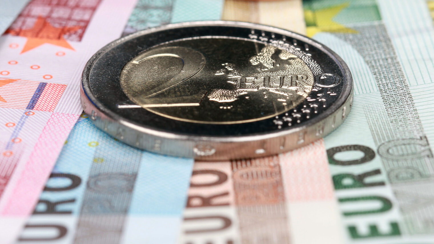 Eine 2-Euro-Münze liegt auf mehreren aufgefächerten Euro-Geldscheinen.