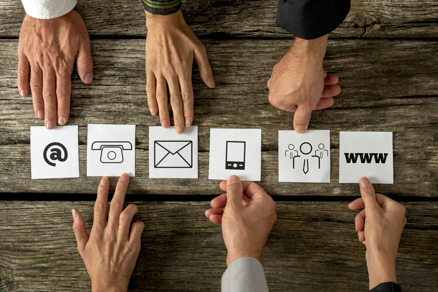 Hände die auf Icons für E-Mail, Telefon, Brief, Handy, Internet und Natur zeigen.