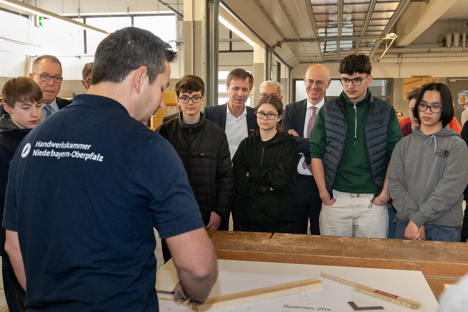 Ausbilder erklärt Schülern anhand Holzmaterialien wie ein Dachstuhl aussieht. 