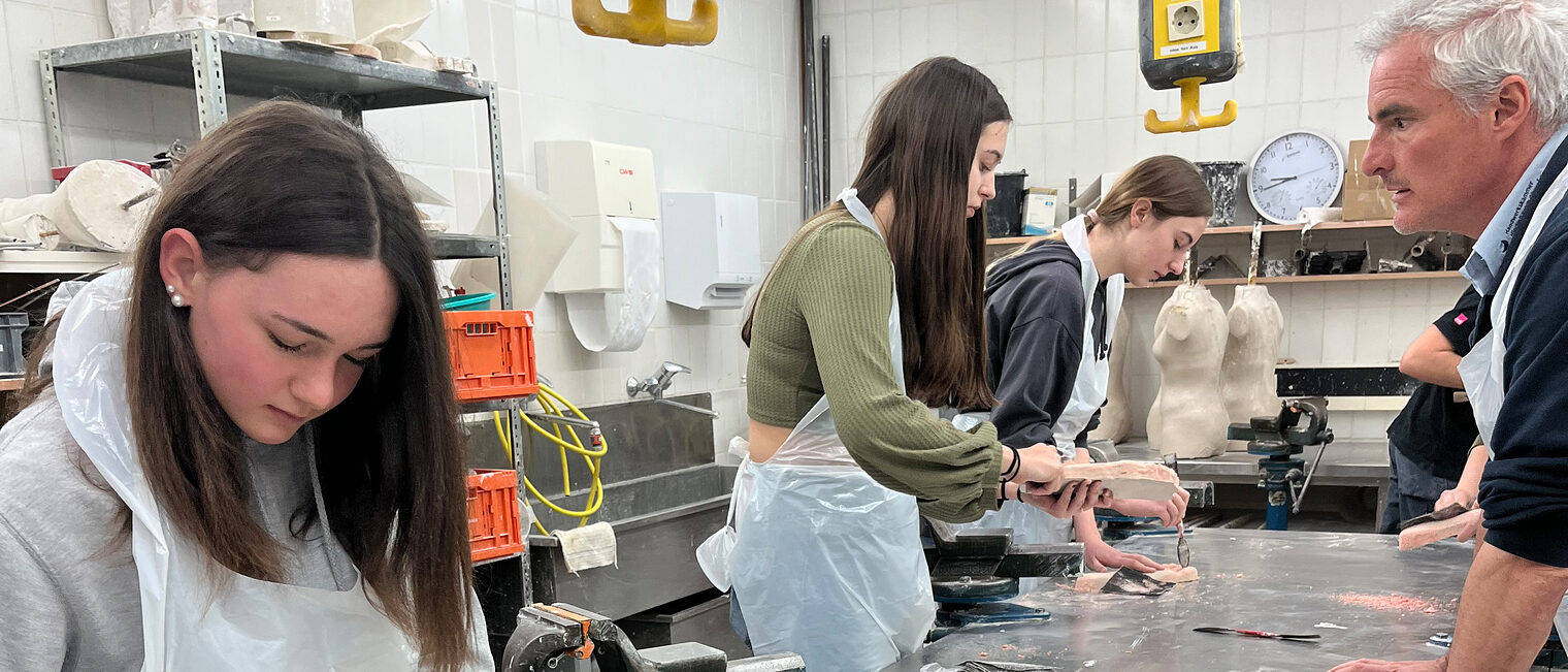In der Orthopädietechnik modellierten die Schülerinnen und Schüler ihre eigenen Füße und lernten gleichzeitig was hinter dem Beruf des Orthopädieschuhmachers steckt. Schülerinen mit Schutzkittel bekleidet formen Fußeinlagen.
