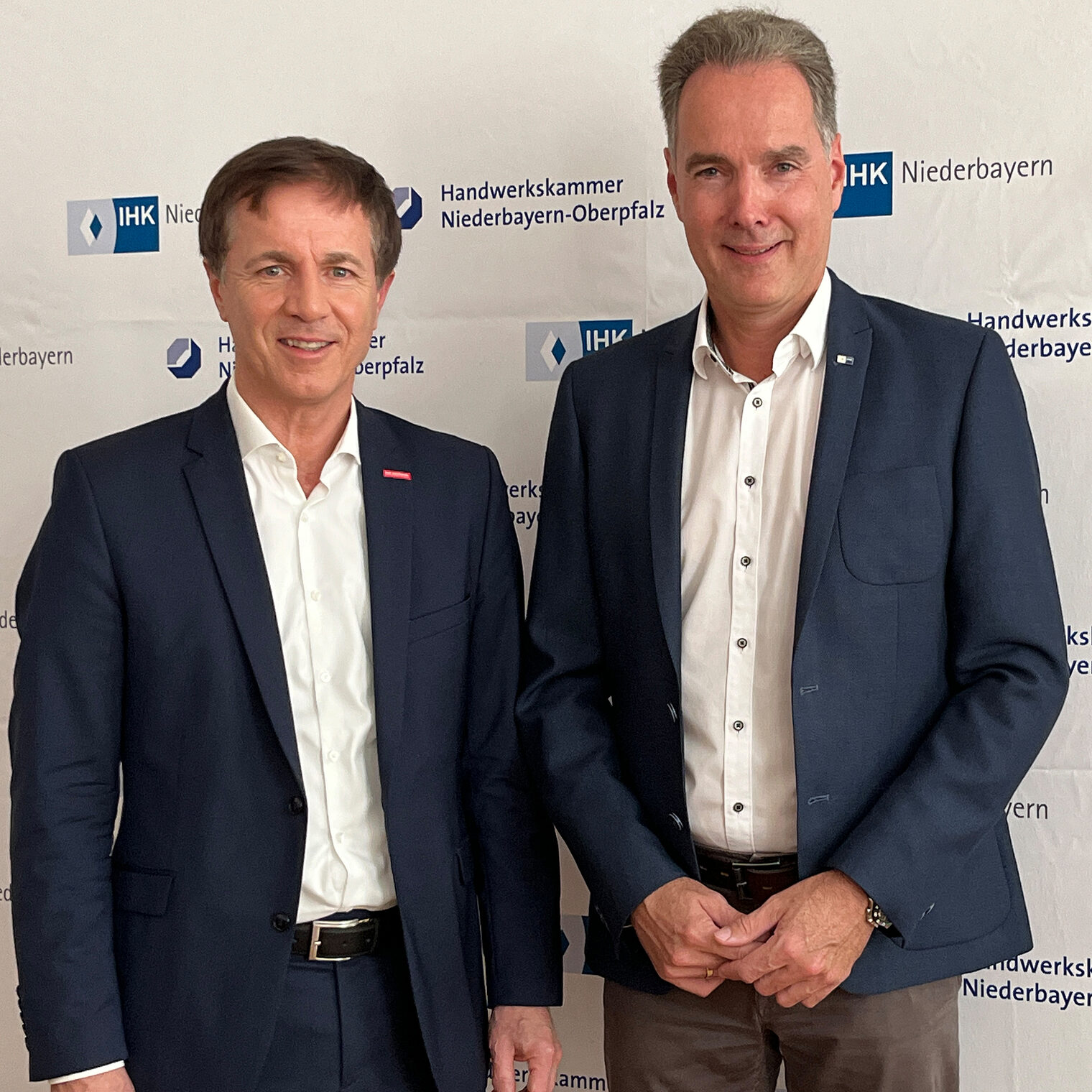 Die Hauptgeschäftsführer der Handwerkskammer und der IHK Niederbayern stehen vor einer Pressewand. 