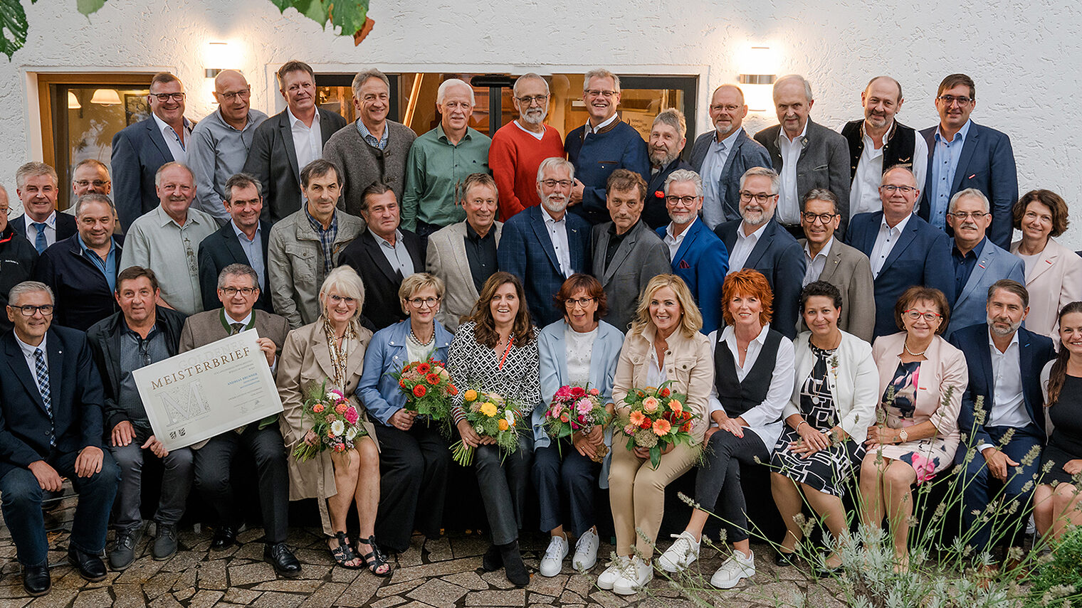 Die 33 Goldenen Meister freuen sich mit den Ehrengästen über ihren Meisterbrief. Fünf Damen halten zusätzlich noch Blumensträuße in den Händen. 