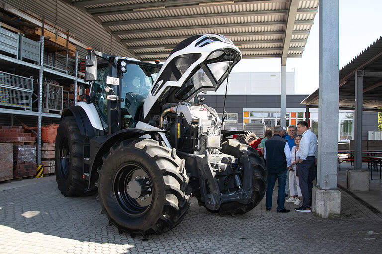Die Motorhaube des Traktors der Innung für Land- & Baumaschinentechnik wurde geöffnet, einige Menschen stehen interessiert daneben. 