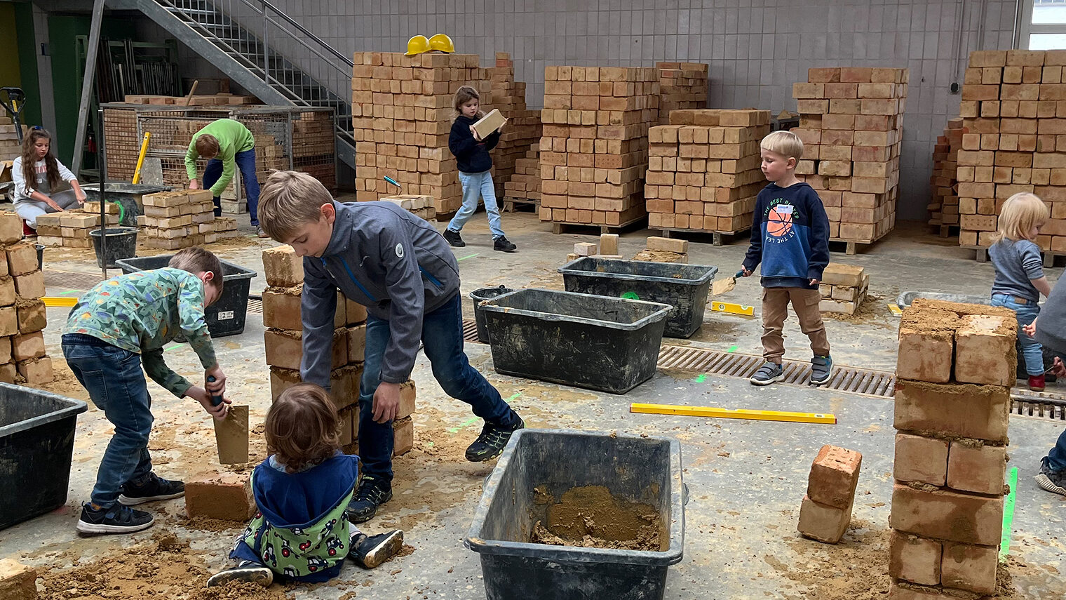 In der Bauhalle versuchen sich viele Kinder daran, Ziegelsteine mit Beton zu mauern. 