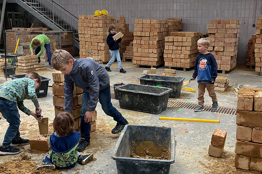In der Bauhalle versuchen sich viele Kinder daran, Ziegelsteine mit Beton zu mauern. 