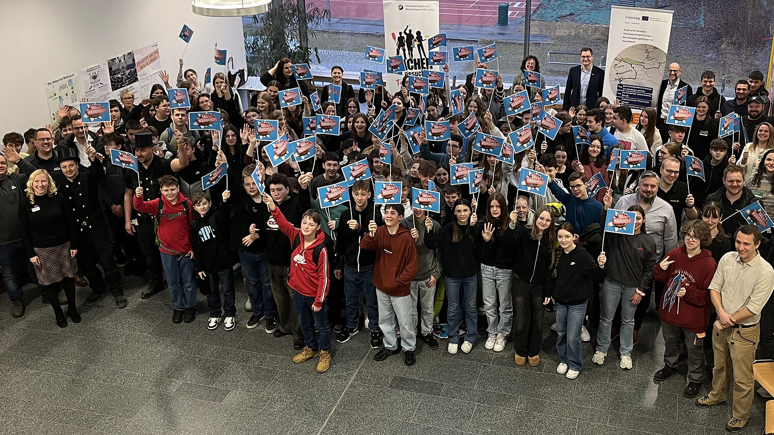Die 120 Schülerinnen und Schüler in der Aula der Realschule. Alle halten Handwerks-Fahnen in die Luft.
