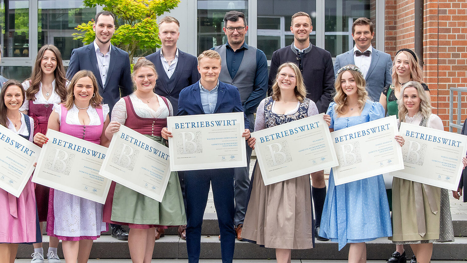 Die Betriebswirte halten fröhlich ihre Zeugnisse in die Kamera. Die Ehrengäste freuen sich mit ihnen. 