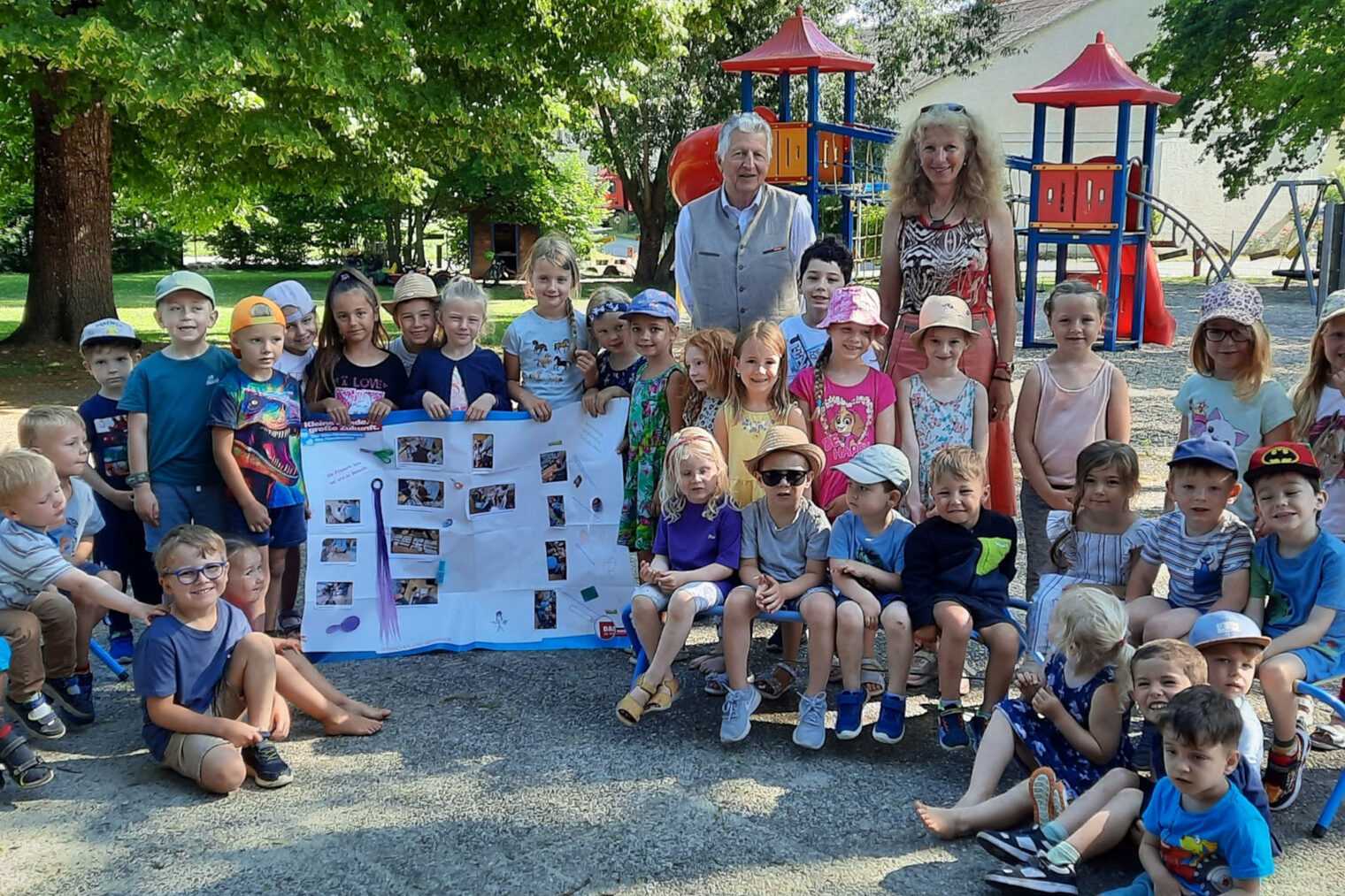 HWK-Vizepräsident Hans Kastl besuchte die Kinder des Kindergartens der Spitalstiftung Irlbach. Eine Kindergartengruppe des Kindergartens Irlbach steht mit einer Erzieherin und HWK-Vizepräsident Hans Kastl im Garten vor einem Kletterturm und halten ein Plakat hoch.