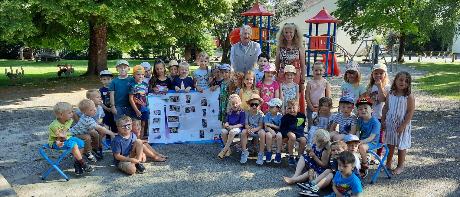 HWK-Vizepräsident Hans Kastl besuchte die Kinder des Kindergartens der Spitalstiftung Irlbach. Eine Kindergartengruppe des Kindergartens Irlbach steht mit einer Erzieherin und HWK-Vizepräsident Hans Kastl im Garten vor einem Kletterturm und halten ein Plakat hoch.