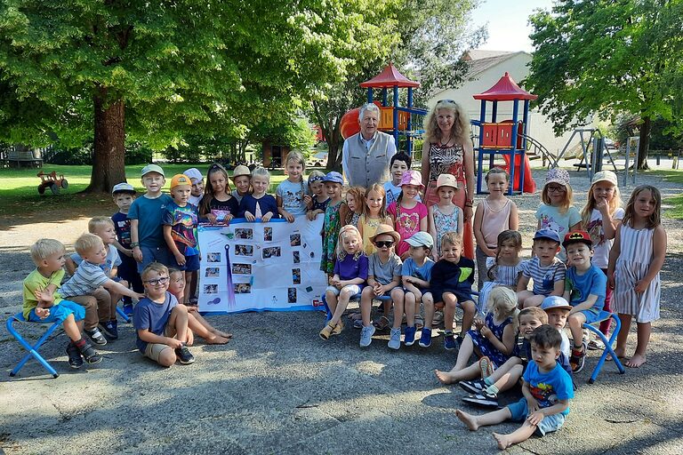 Eine Kindergartengruppe des Kindergartens Irlbach steht mit einer Erzieherin und HWK-Vizepräsident Hans Kastl im Garten vor einem Kletterturm und halten ein Plakat hoch.