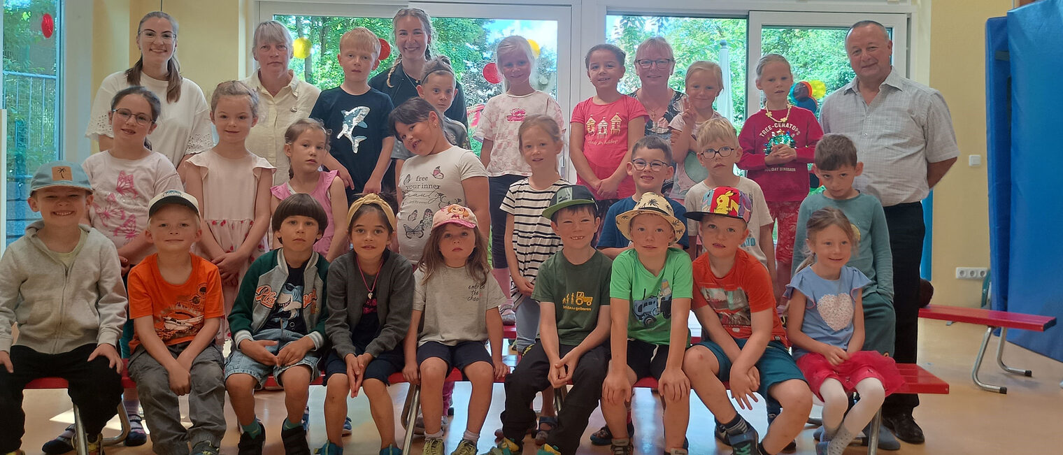 HWK-Vizepräsident Christian Läpple (rechts) zu Besuch beim Kindergarten „Bergzwergerl“. Die Kindergartengruppe, Erwachsene und HWK-Vizepräsident Christian Läpple stehen und sitzen in einem Raum mit großen Fenstern.