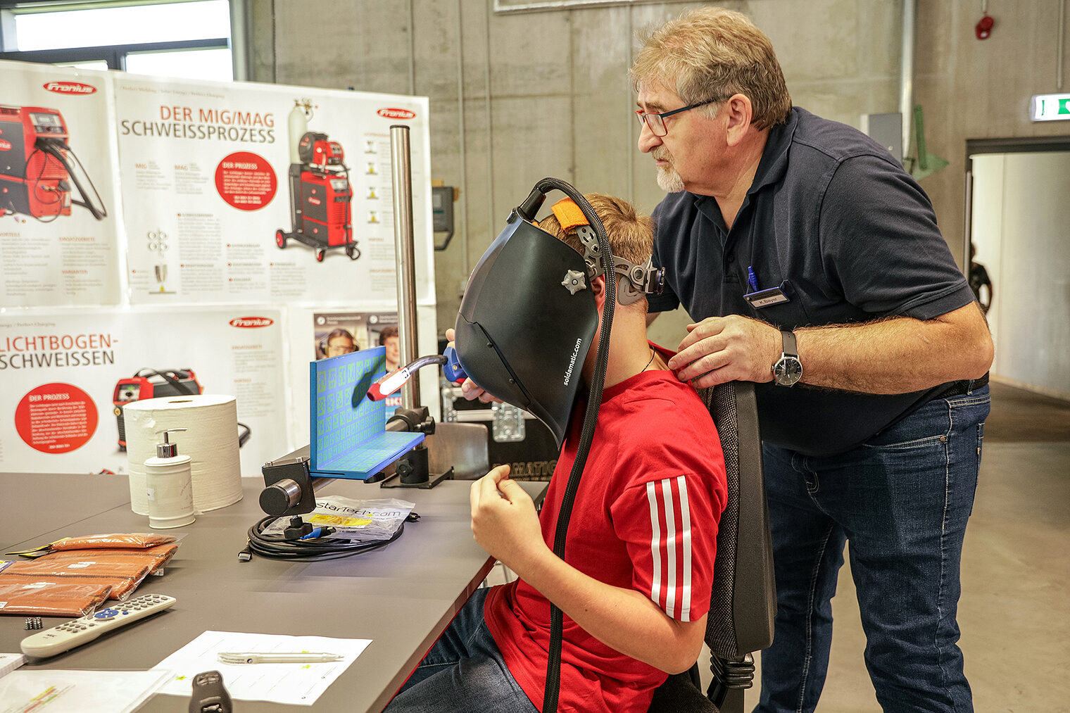 Ein Jugendlicher probiert sich aus beim virtuellen Schweißen. Der Ausbilder unterstützt ihn dabei. 