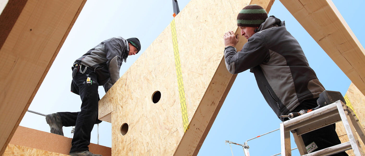 Zwei Zimmerer stellen einen Dachstuhl auf. 
