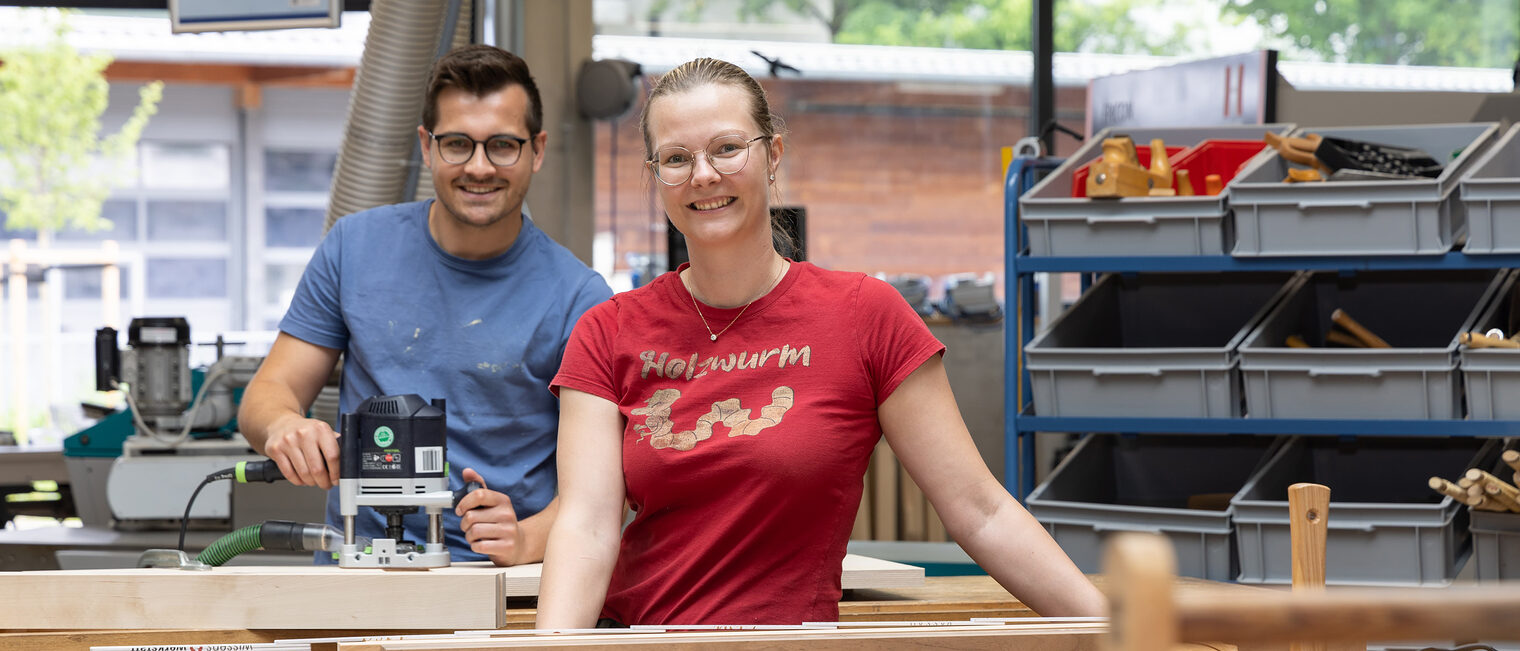 Ein Meisterschüler und eine Meisterschülerin arbeiten mit Freude an der Schreiner-Werkbank.