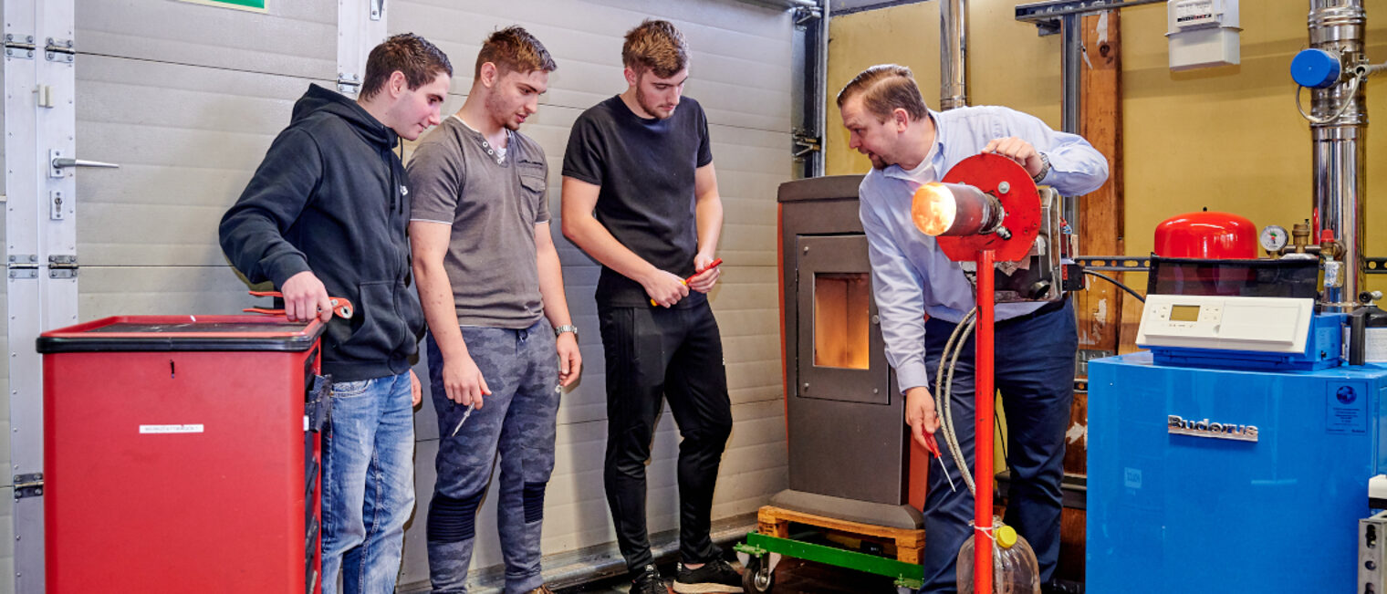 Drei Auszubildende für Sanitär,- Heizungs- und Klimatechnik erhalten eine Unterweisung von einem Ausbilder.