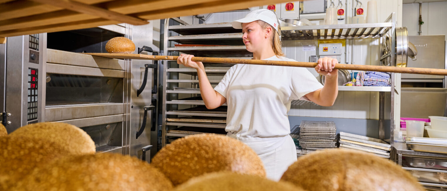 Eine Auszubildende holt ein Laib Brot aus dem Ofen.