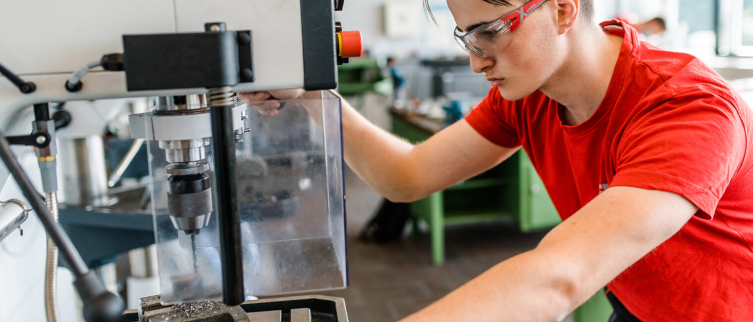 Auszubildender steht an der Bohrmaschine.