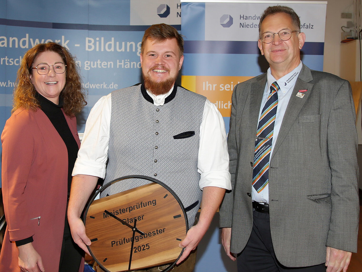 Josef Siglreithmaier wurde mit seiner besonderen Uhr als bester Prüfling in Theorie und Praxis geehrt. Josef Siglreithmaier zeigt stolz sein Meisterstück in die Kamera. Mit auf dem Foto Vizepräsidetin Claudia Geiselhöringer und Josef Sailer.