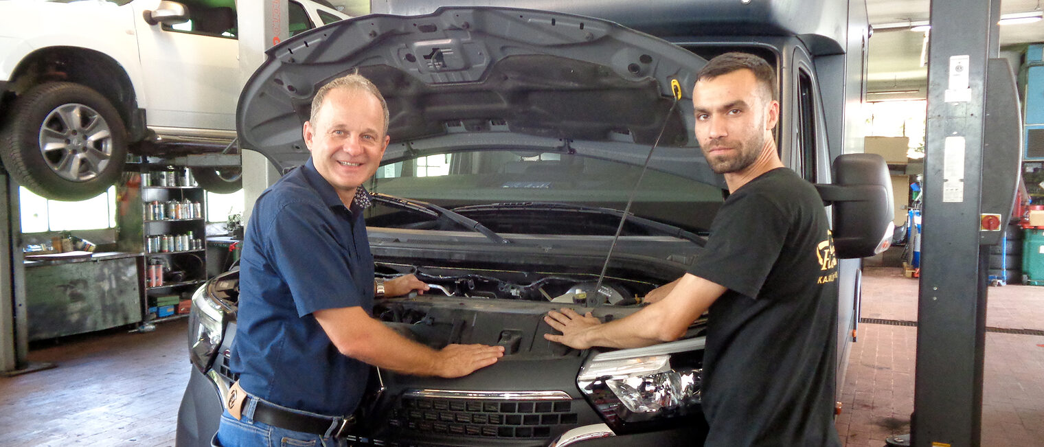 Omid Vahdani mit seinem Lehrmeister Wolfgang Feldmeier in dessen Werkstatt, sie arbeiten an einem Auto. 