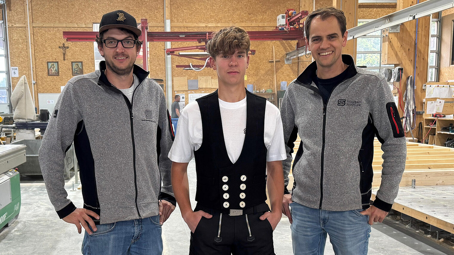 Mathias Schmid steht mittig. Er startet nächstes Jahr seine Ausbildung als Zimmerer. Geschäftsführer und Ausbildungsleiter stehen stolz neben ihm. 