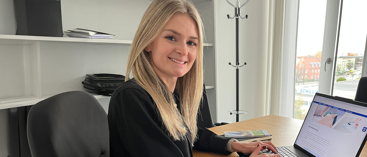 Corinna Dobmeier unterstützt die Betriebsberatung. Sie sitzt in ihrem Büro vor dem Laptop und lächelt in die Kamera.