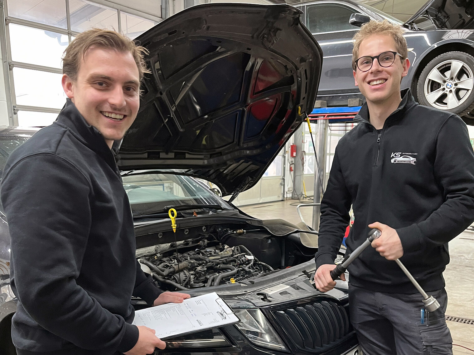 Die beiden neuen, jungen Inhaber von „KS Automobile“ stehen vor einer geöffneten Motorhaube. Sie sind seit kurzem ihr eigener Chef. 