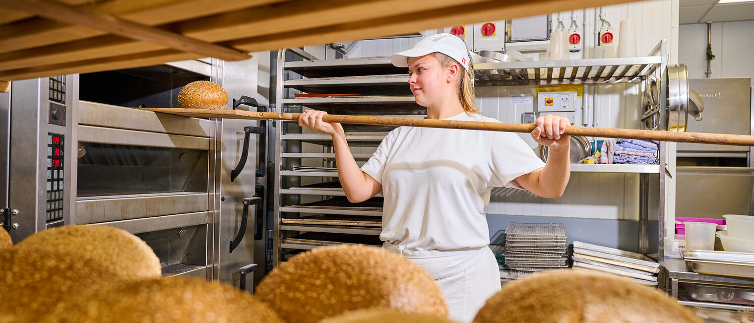 Eine junge Bäckerin schiebt holt mit gerade ein frischgebackenes Brot aus dem Ofen.