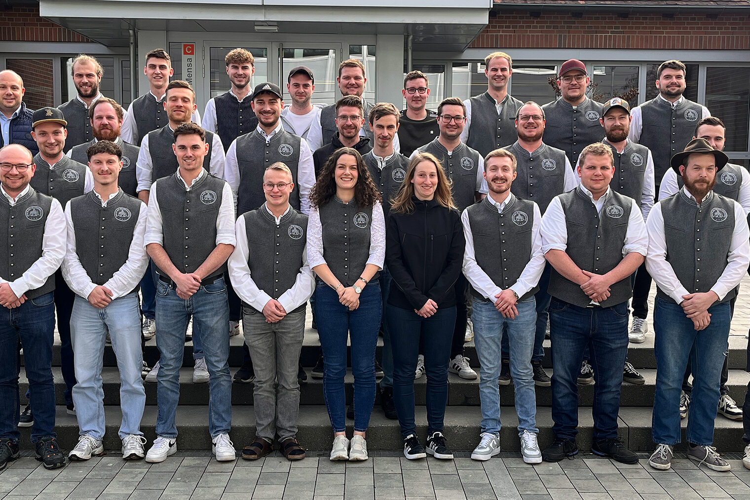 Die Teilnehmer des Meisterkurses posieren stolz vor dem Bildungszentrum in Regensburg. Sie haben ihre Maurerkluft an.