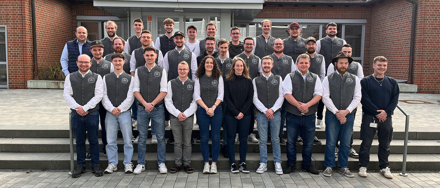 Die Teilnehmer des Meisterkurses posieren stolz vor dem Bildungszentrum in Regensburg. Sie haben ihre Maurerkluft an.