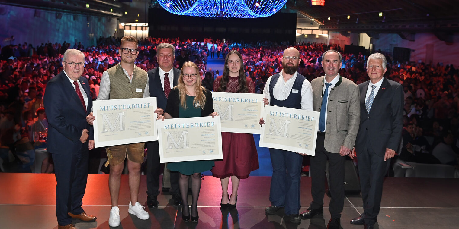 Vier Meister erhalten auf der Bühne ihre Meisterbriefe von Staatsminister Hubert Aiwanger und Hauptgeschäftsführer Jürgen Kilger.